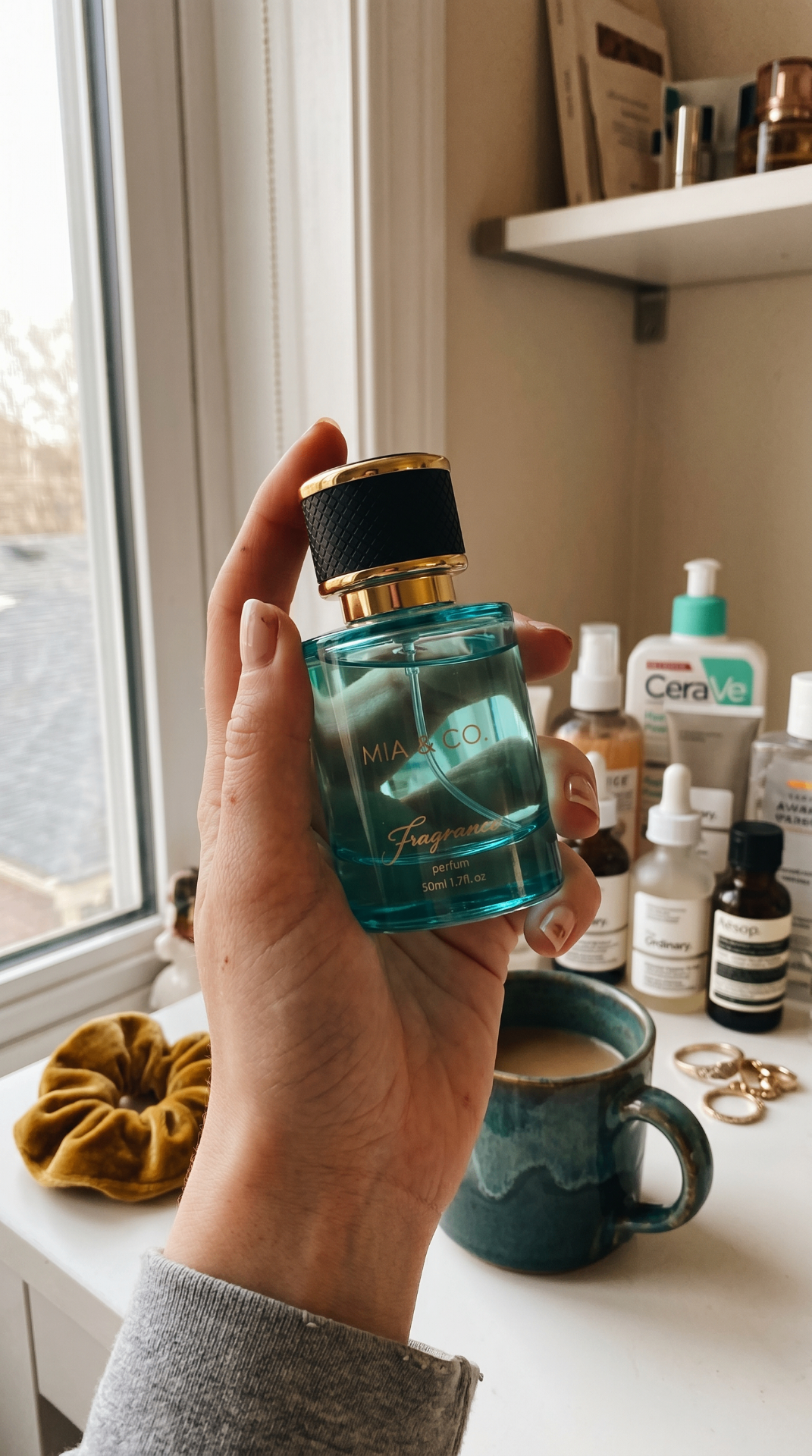 Mia & Co. teal fragrance bottle held in hand by a sunlit window